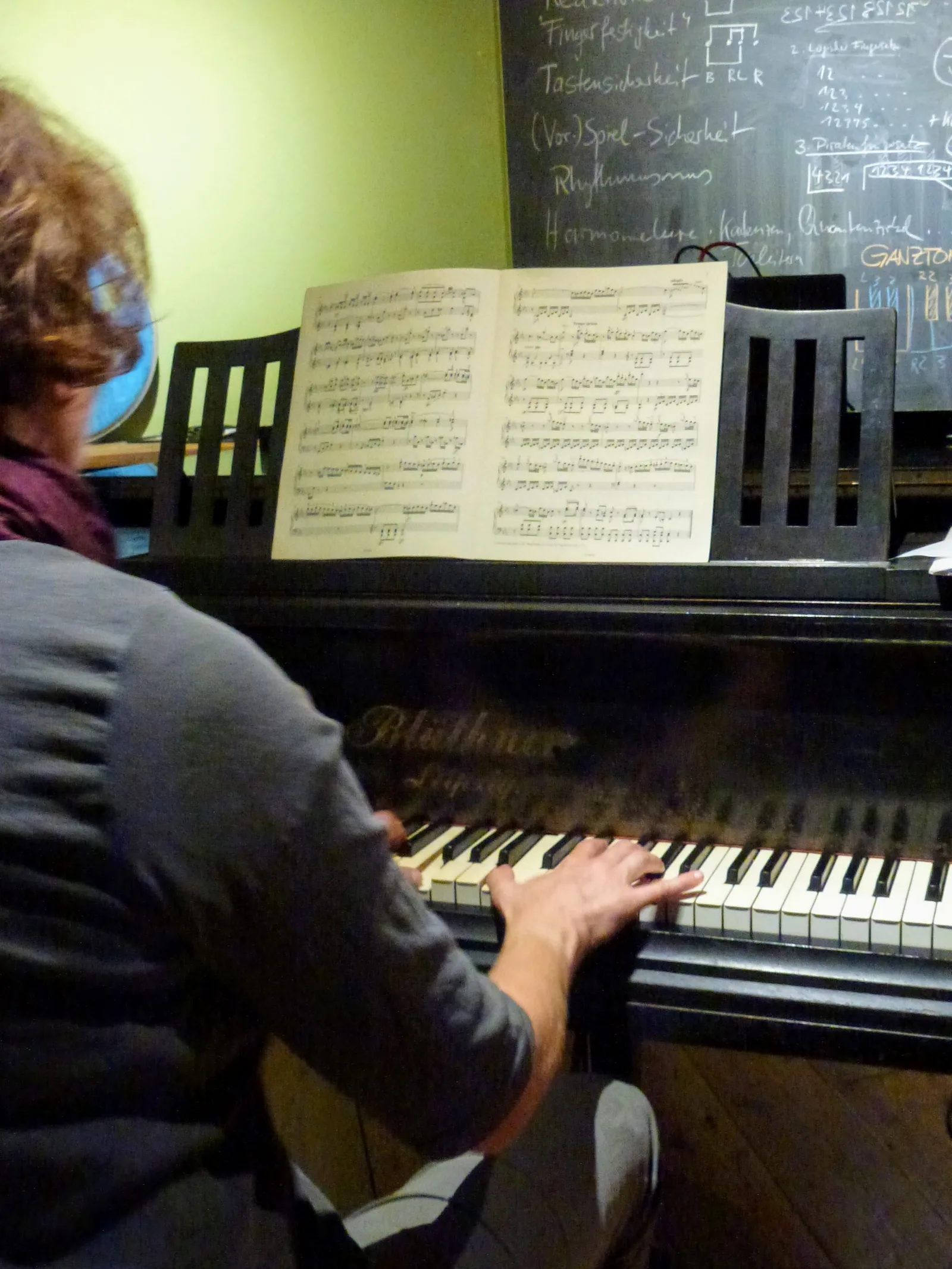 Schüler spielt Klavier nach Noten mit Tafel im Hintergrund
