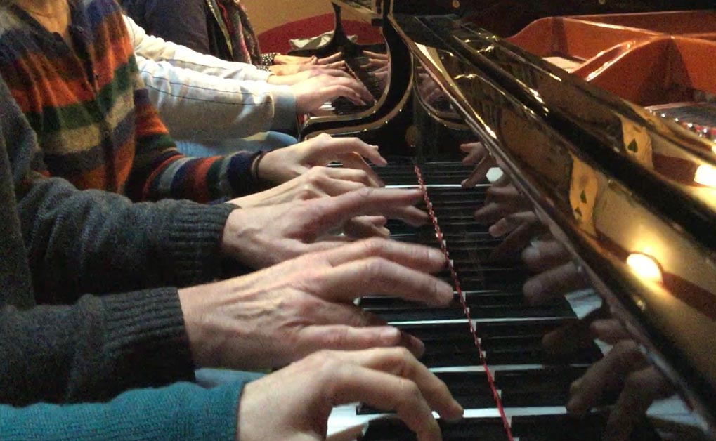Mehrere Hände tasten gemeinsam auf Klaviertasten, Nahaufnahme von oben