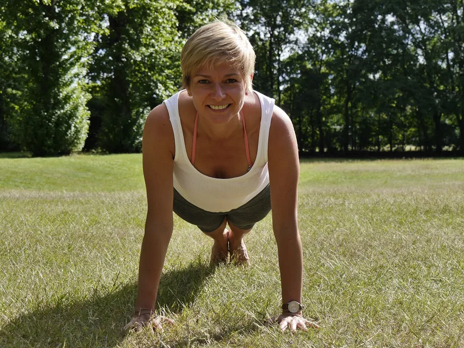 Endlich Migränefrei – Online-Coaching gegen Migräne von Anke Schneider 23 Anke Schneider in Plank-Position auf grüner Wiese vor Bäumen