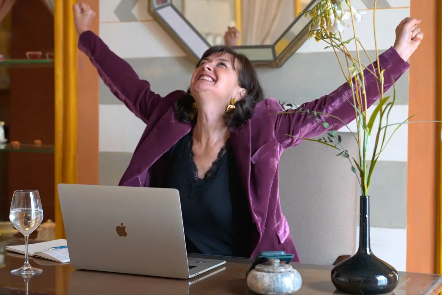 Andrea Randt in violettem Blazer vor Laptop, Arme erhoben in Siegespose, erfolgreiches Business