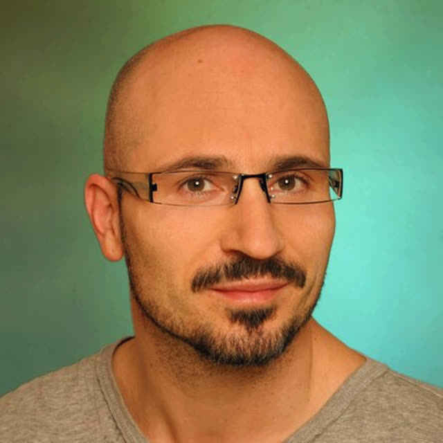 Dr. Jens Barthel Mann, Glatze, Brille, Bart, beiges Shirt vor türkisem Hintergrund