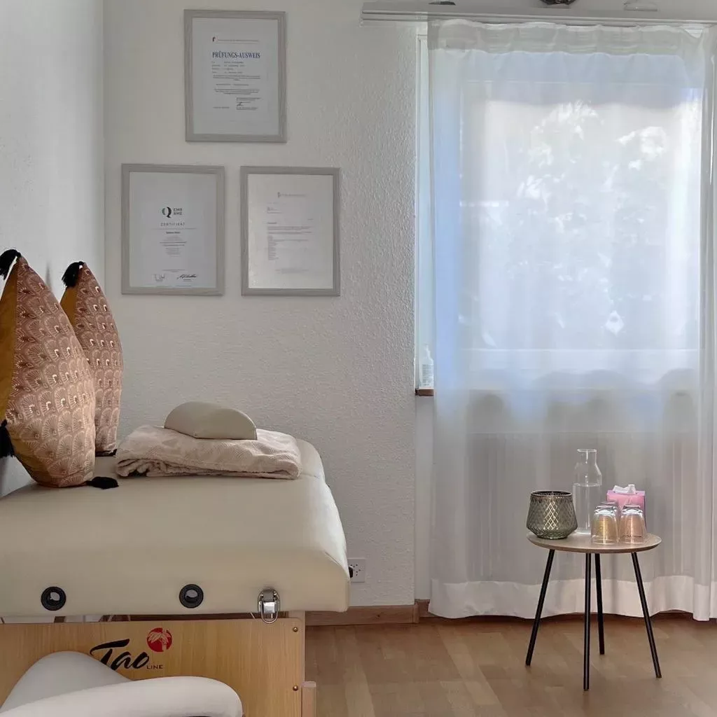 Massage-Liege mit Kissen, Praxisraum mit Prüfungszertifikaten an der Wand