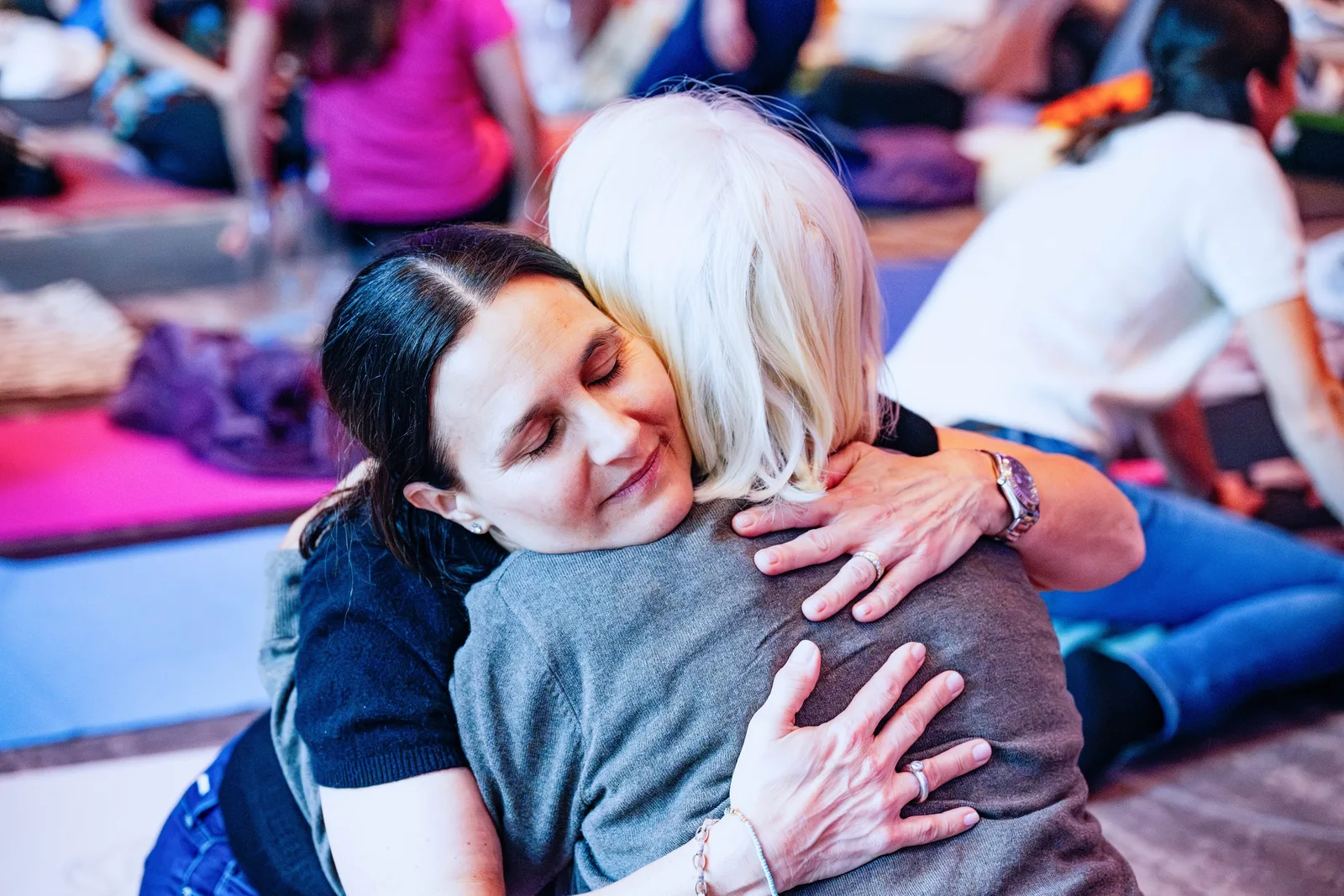 Energetische Heilung Community von Julia Gössler 12 Zwei Frauen umarmen sich herzlich in Trainingsumgebung mit Publikum