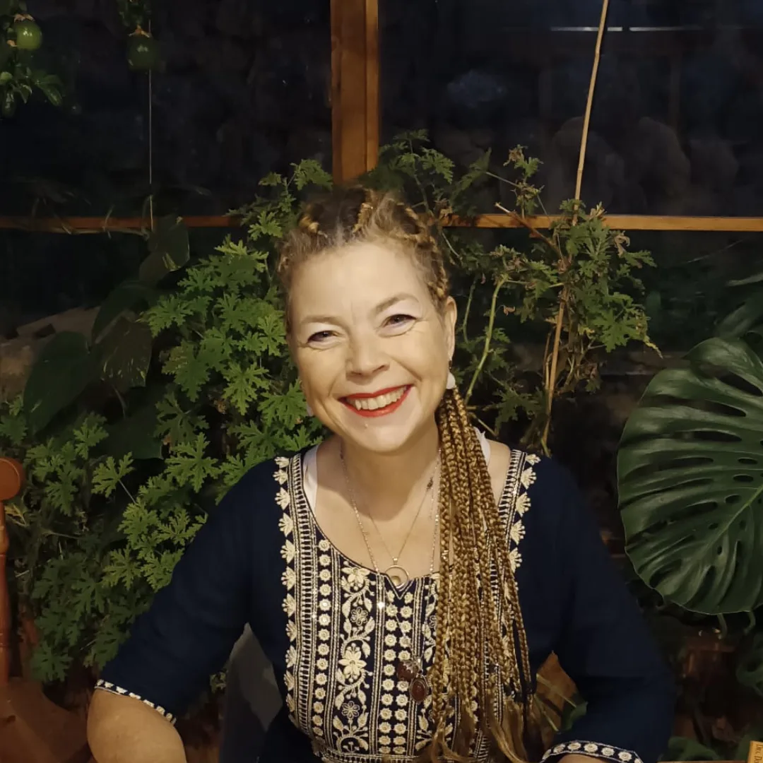 Porträt lächelnde Frau mit geflochtenen Haaren, Boho-Kleidung, Pflanzen im Hintergrund