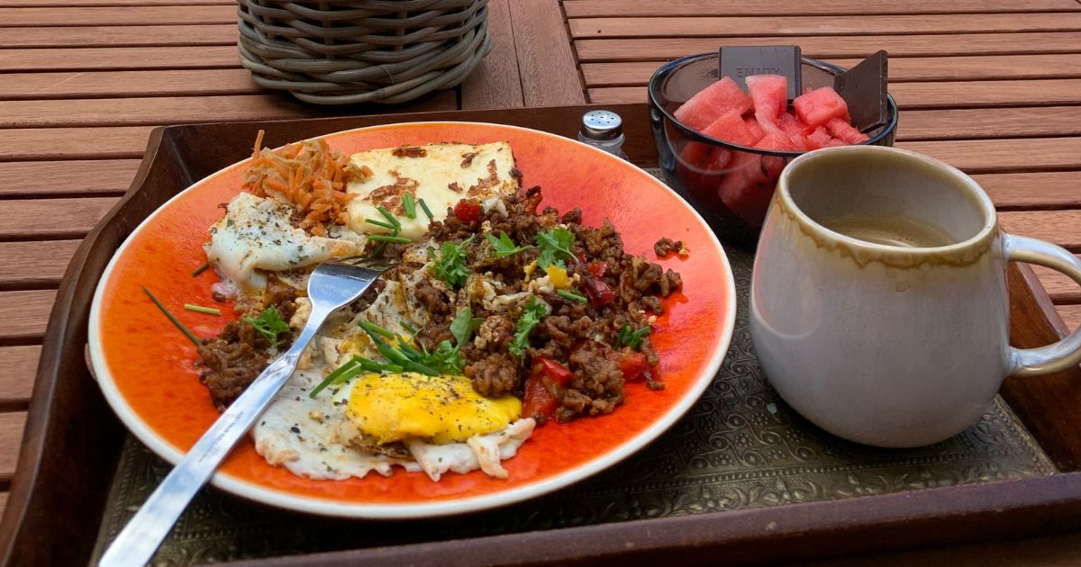 Real Food Frühstück mit Ei, Hackfleisch, Gemüse auf orangem Teller, Kaffee auf Holztisch