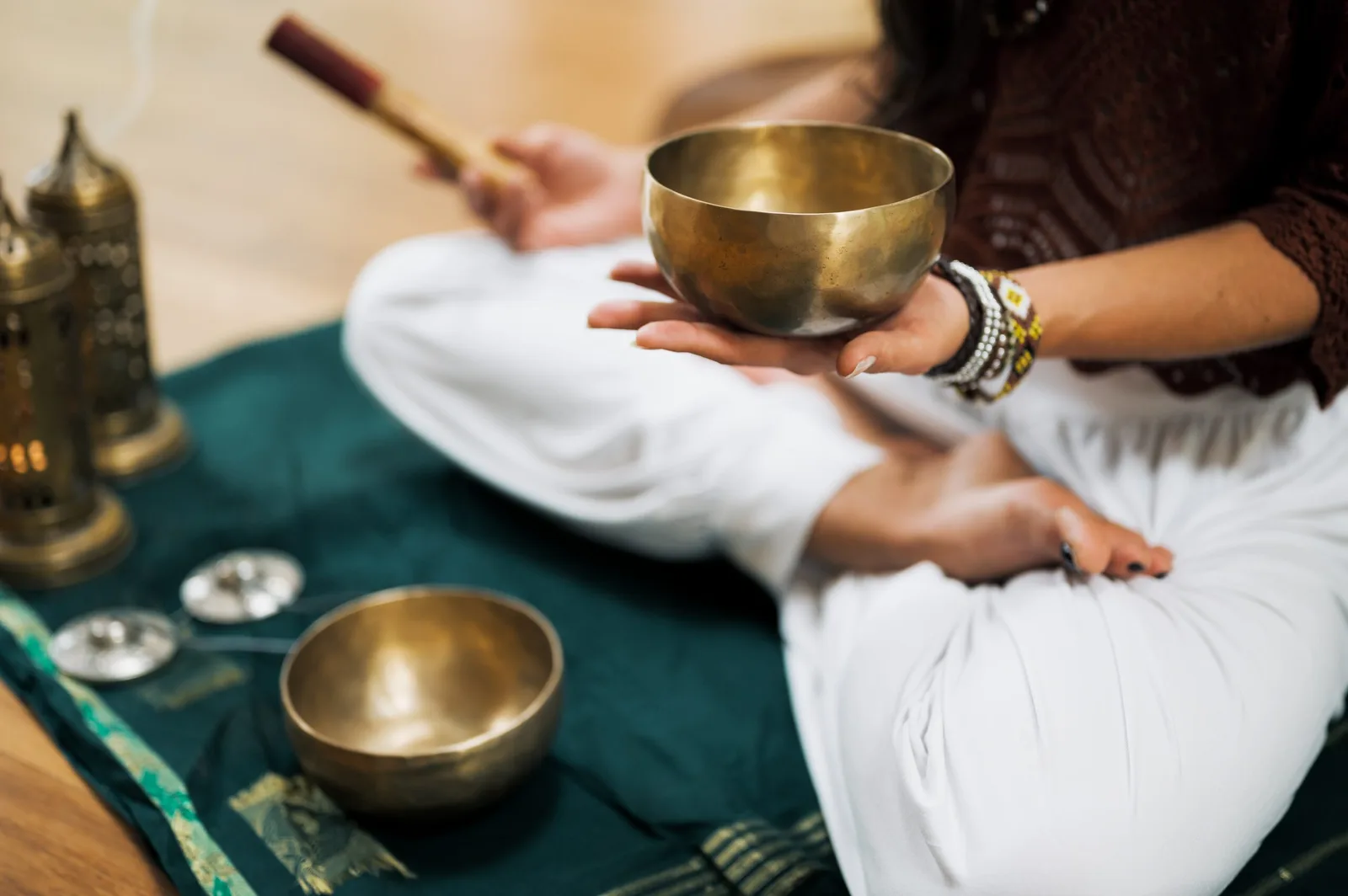 Entfalte den Meister in dir! – Meditationen und Klangreisen 6 Hände halten goldene Klangschale über grünem Tuch, weißes Meditationskissen, Klöppel und Räuchergefäße im Hintergrund