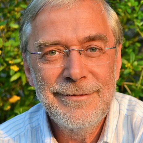 Porträt von Dr. Gerald Hüther, älterer Mann mit Brille vor grünem Hintergrund