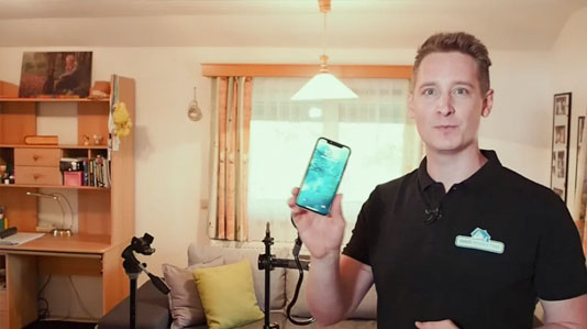 Erfolgreiche Immobilien Fotos – Objektbilder-Kurs von Alex Stadler 12 Mann zeigt Smartphone-Display mit Wohnzimmer im Hintergrund und Stativ
