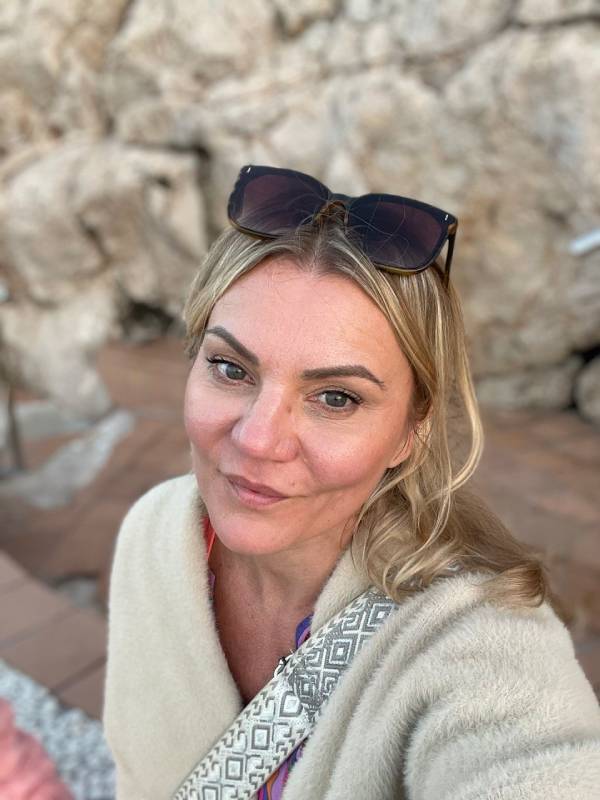 Blonde Frau mit Sonnenbrille vor steiniger Wand, porträtiert in Nahaufnahme