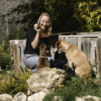 Doris Raemisch mit zwei braunen Hunden in Garten vor Holztor