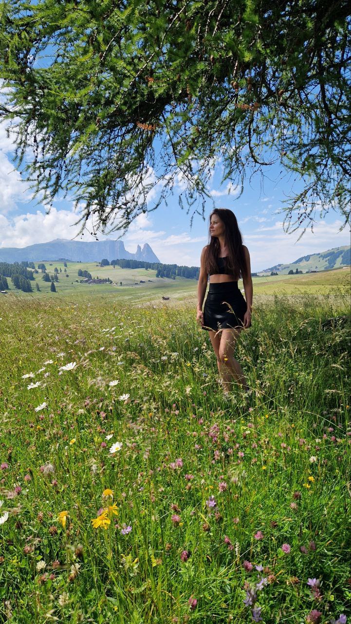 Frau auf blühender Almwiese unter Baum, Berglandschaft mit Dolomiten im Hintergrund