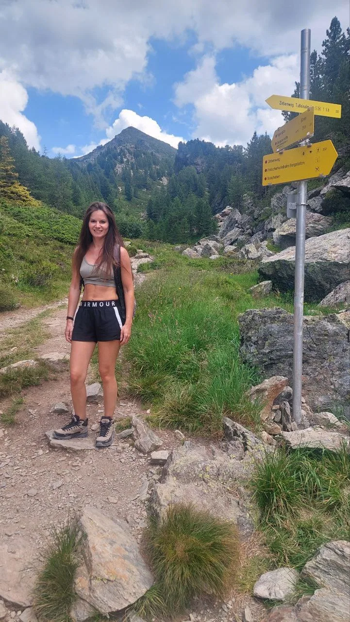 Nina Muigg beim Wandern auf Bergweg mit Wegweiser, Alpenpanorama