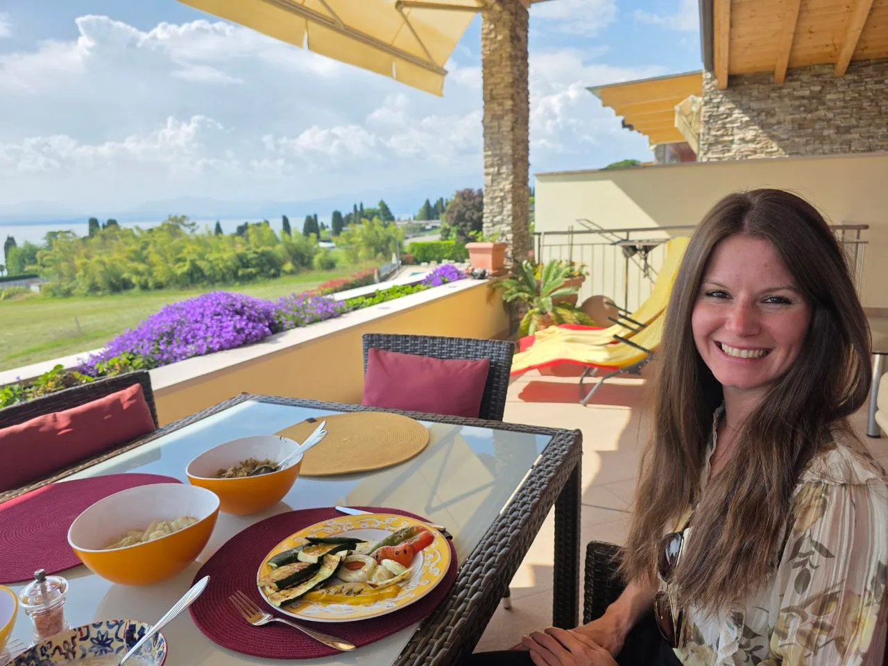 Pflanzliches Mittagessen auf Terrasse mit Seeblick, Frau mit Essen und Lächeln