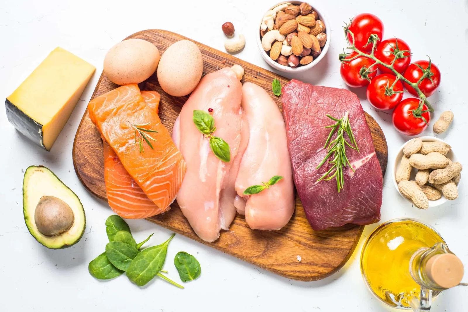 Ketogene Lebensmittel auf weißem Hintergrund: Lachs, Rindfleisch, Huhn, Eier, Käse, Avocado, Nüsse, Tomaten