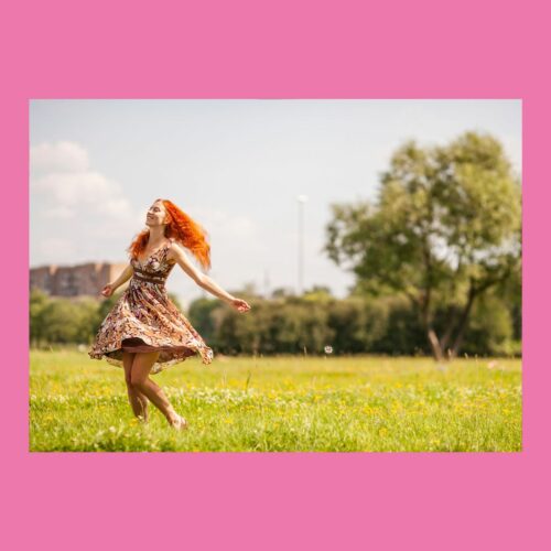 Frau mit orangefarbenen Haaren tanzt auf grüner Wiese im Sonnenlicht