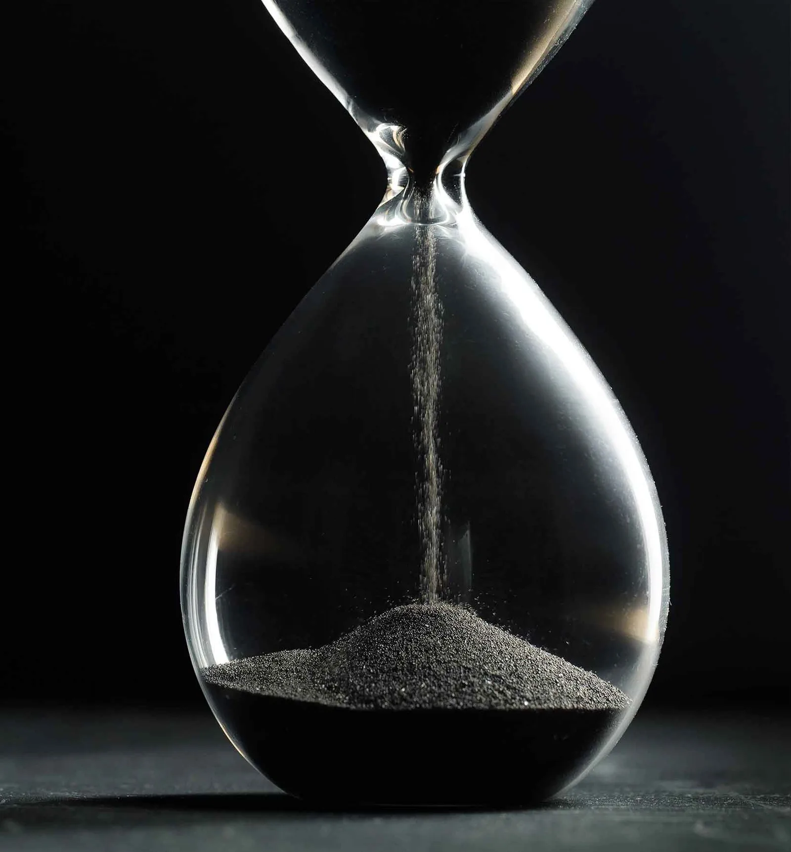 Sanduhr mit schwarzem Hintergrund, Sand läuft durch die Öffnung