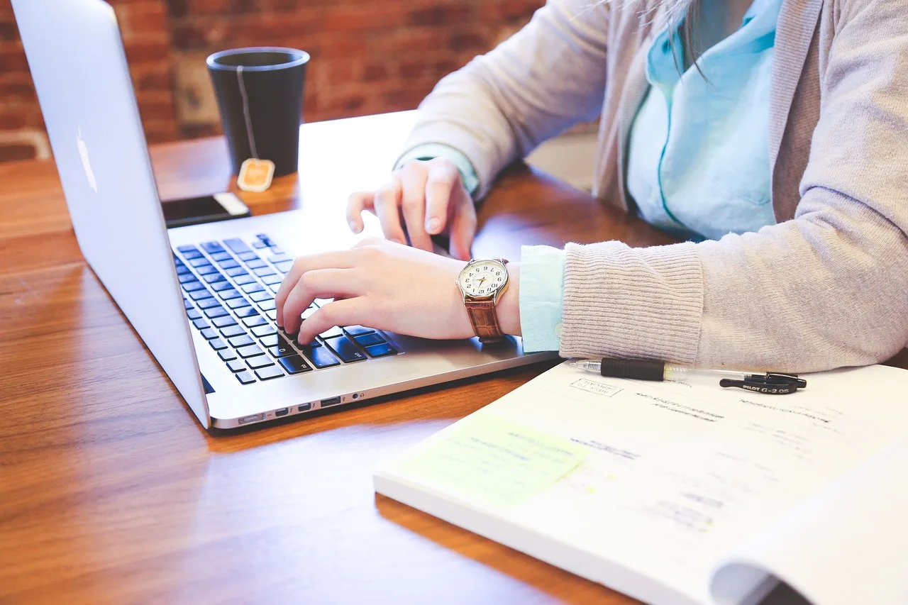 Frauenhände an Laptop-Tastatur mit Kaffee und Notizbuch – Online-Arbeit