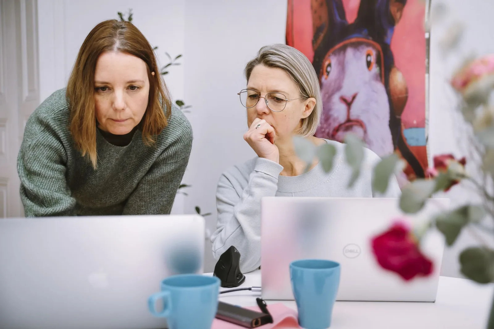 Zwei Frauen konzentriert am Laptop – grüne Pullover und graue Bluse – Coworking