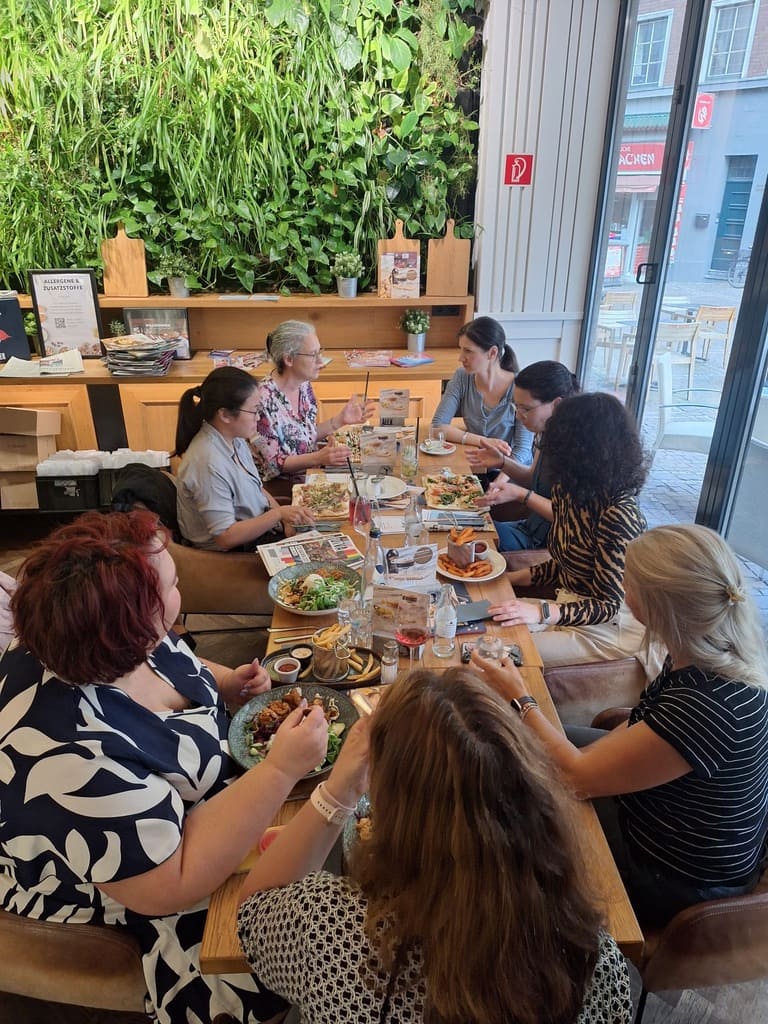 Mehrere Frauen an langer Holztafel mit Speisen im Café – Netzwerkevent