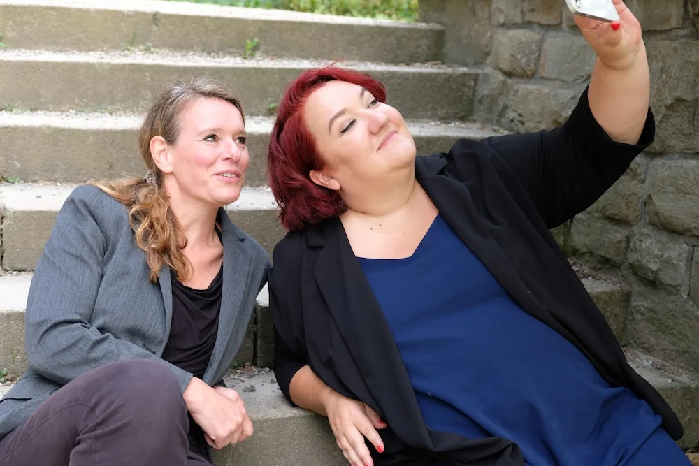 Zwei Unternehmerinnen sitzen auf Steinen, eine macht ein Selfie – Hero-Bild für Frau mit Bizz Mitgliedschaften