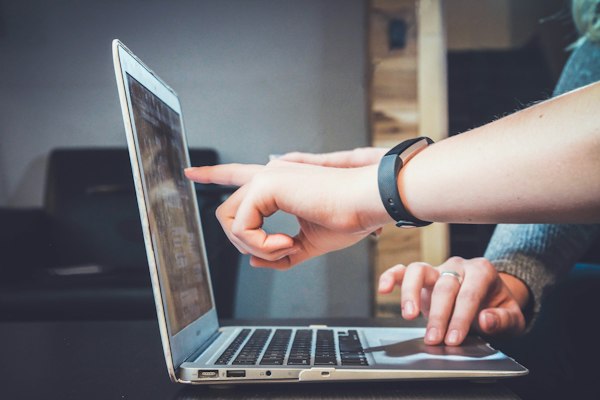 Hände bedienen einen Laptop-Touchpad, Person mit Smartwatch bei der Computernutzung