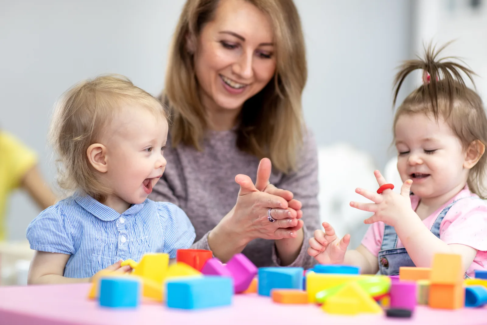 Erzieherin mit zwei Kleinkindern beim Spielen mit bunten Bauklötzen