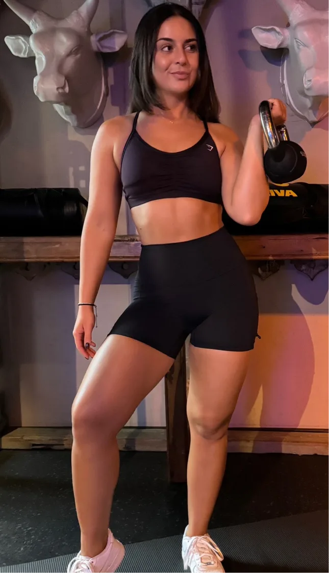 Trainierte Frau mit Hantel in schwarzem Sportoutfit im Fitnessstudio