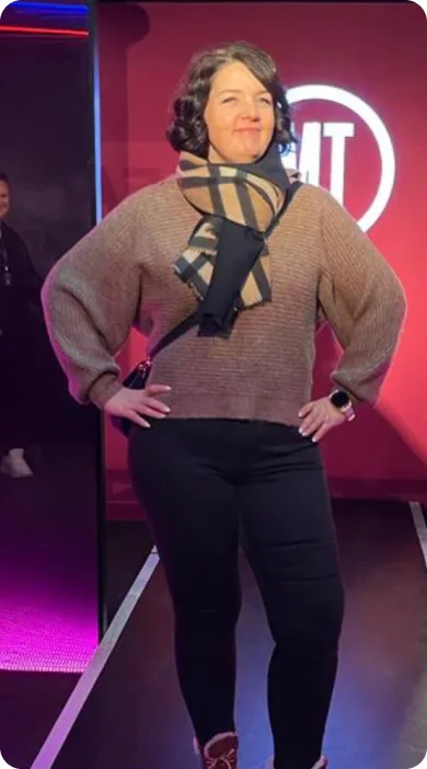 Schlanke Frau in Pullover und schwarzer Hose auf Bühne mit rotem Neon-Hintergrund