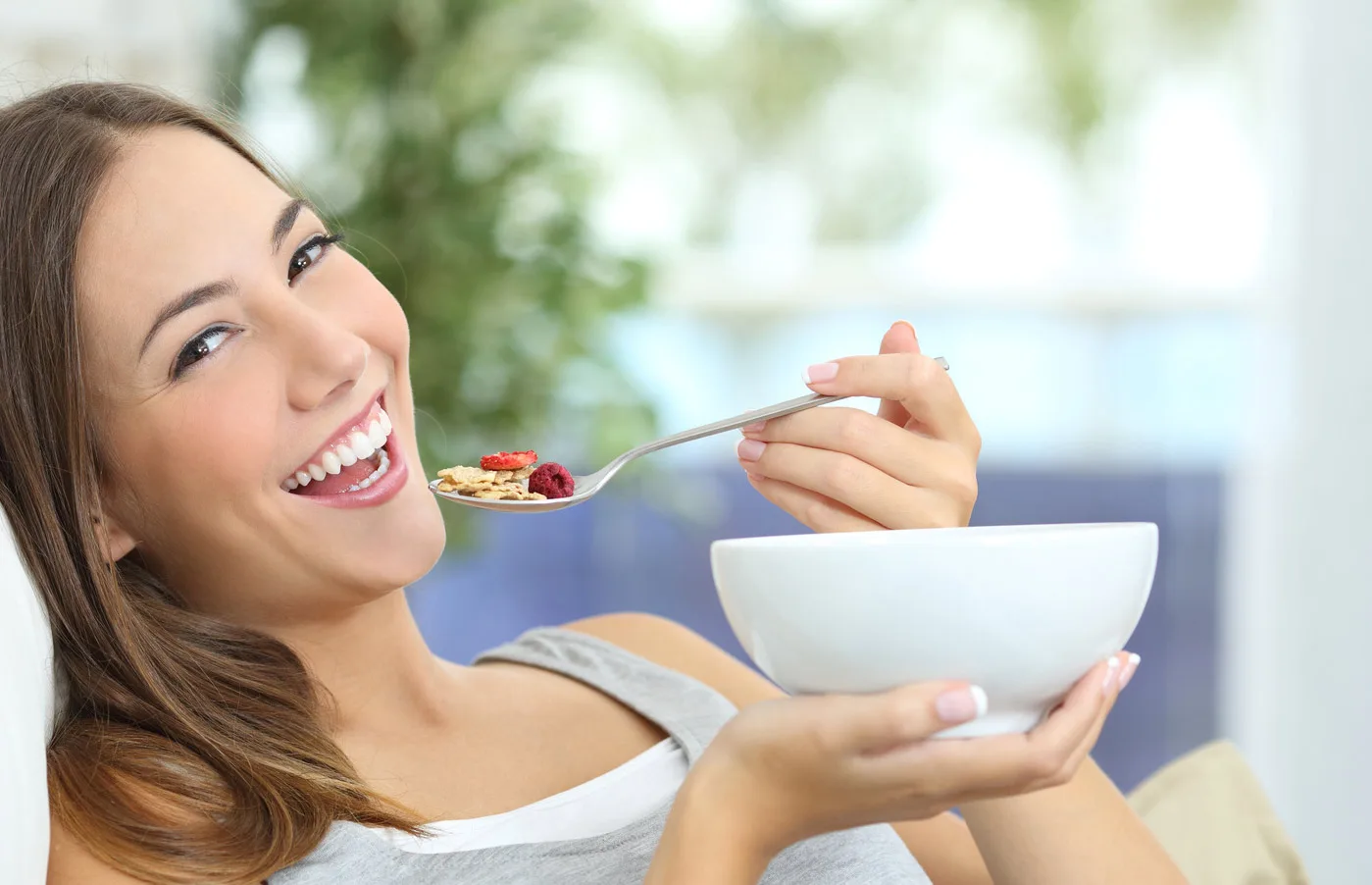 Frau mit Schüssel und Löffel isst fröhlich Müsli mit Früchten
