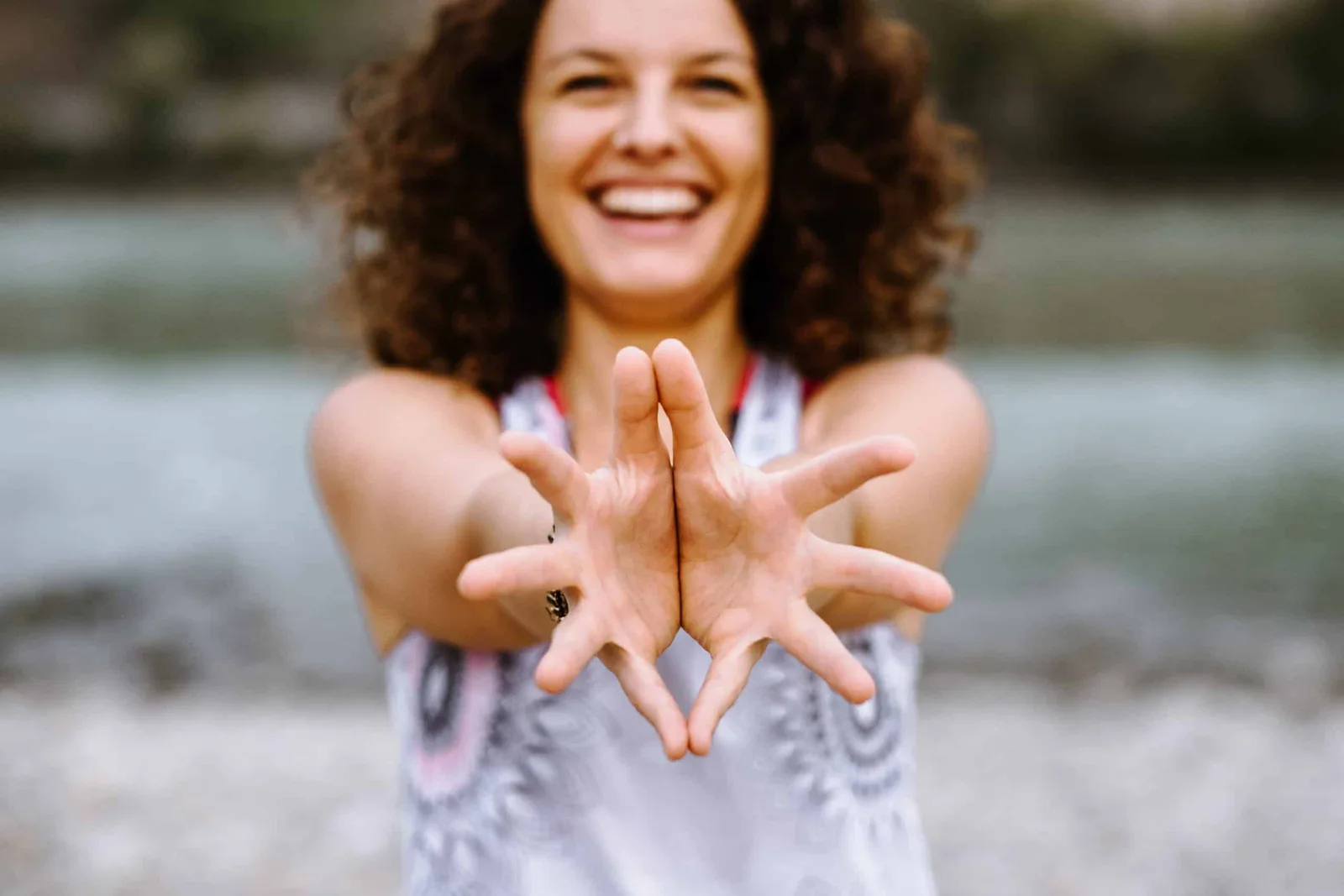 Yoga-Trainerin mit lockigem Haar macht Herzgeste mit beiden Händen am Wasser