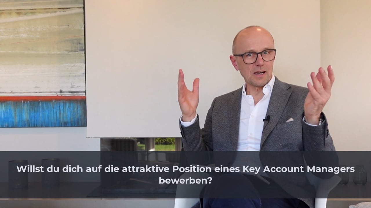 Videostandbild mit Mann in grauem Sakko und Brille, der gestikuliert, mit Frage zum Bewerbungsgespräch als Key Account Manage