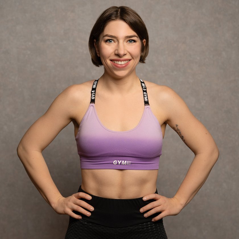 Porträt-Foto von Trainerin Nina Graber in violettem GYMIII Sport-BH vor grauem Hintergrund