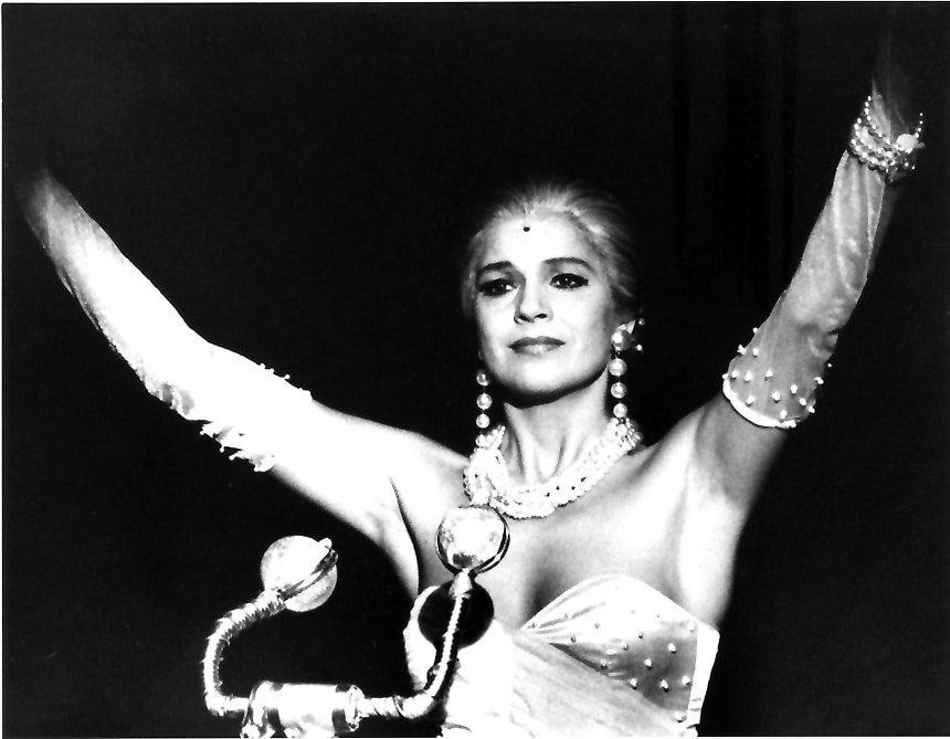 Schwarz-Weiß-Aufnahme von Beatrice Fischer-Stracke als Evita mit Perlenschmuck und erhobenen Armen
