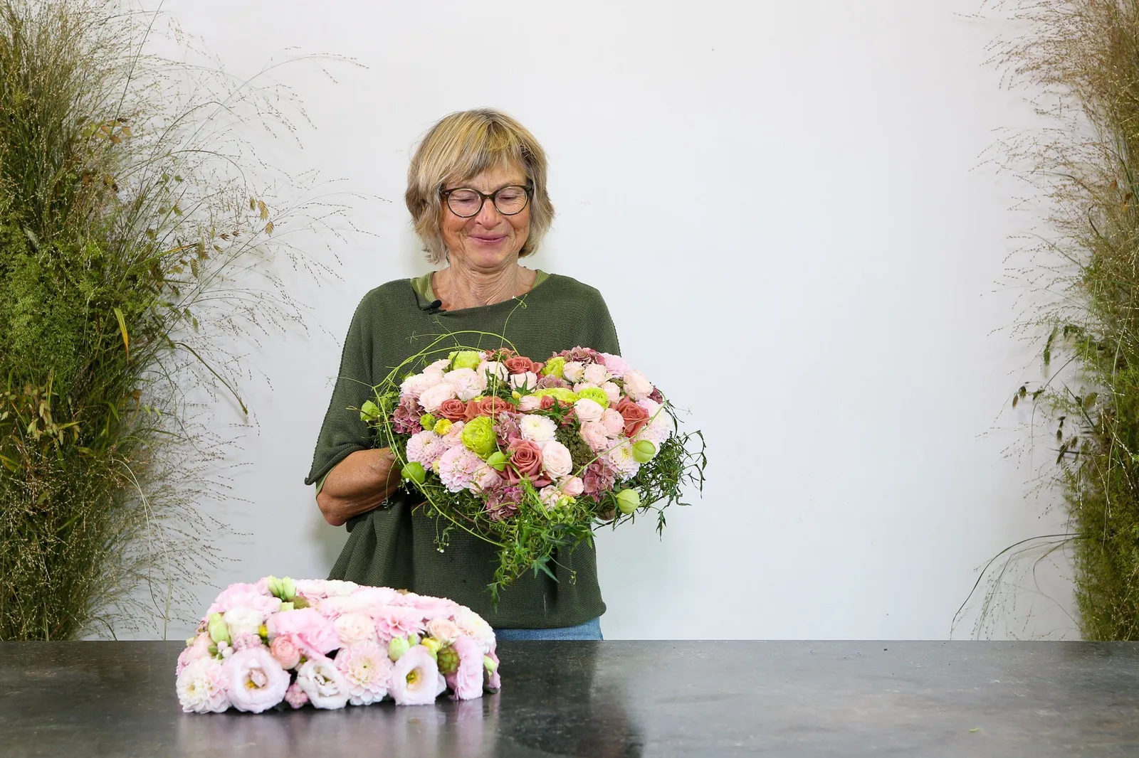 Floristik-Meisterin präsentiert üppige rosa Blumengestaltung mit Rosen, Nelken und Grünwerk