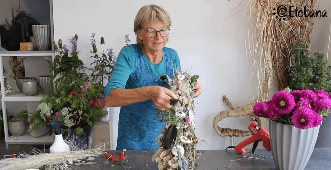 Floristin bindet Trockenblumen-Arrangement mit Gerberas und Naturmaterialien