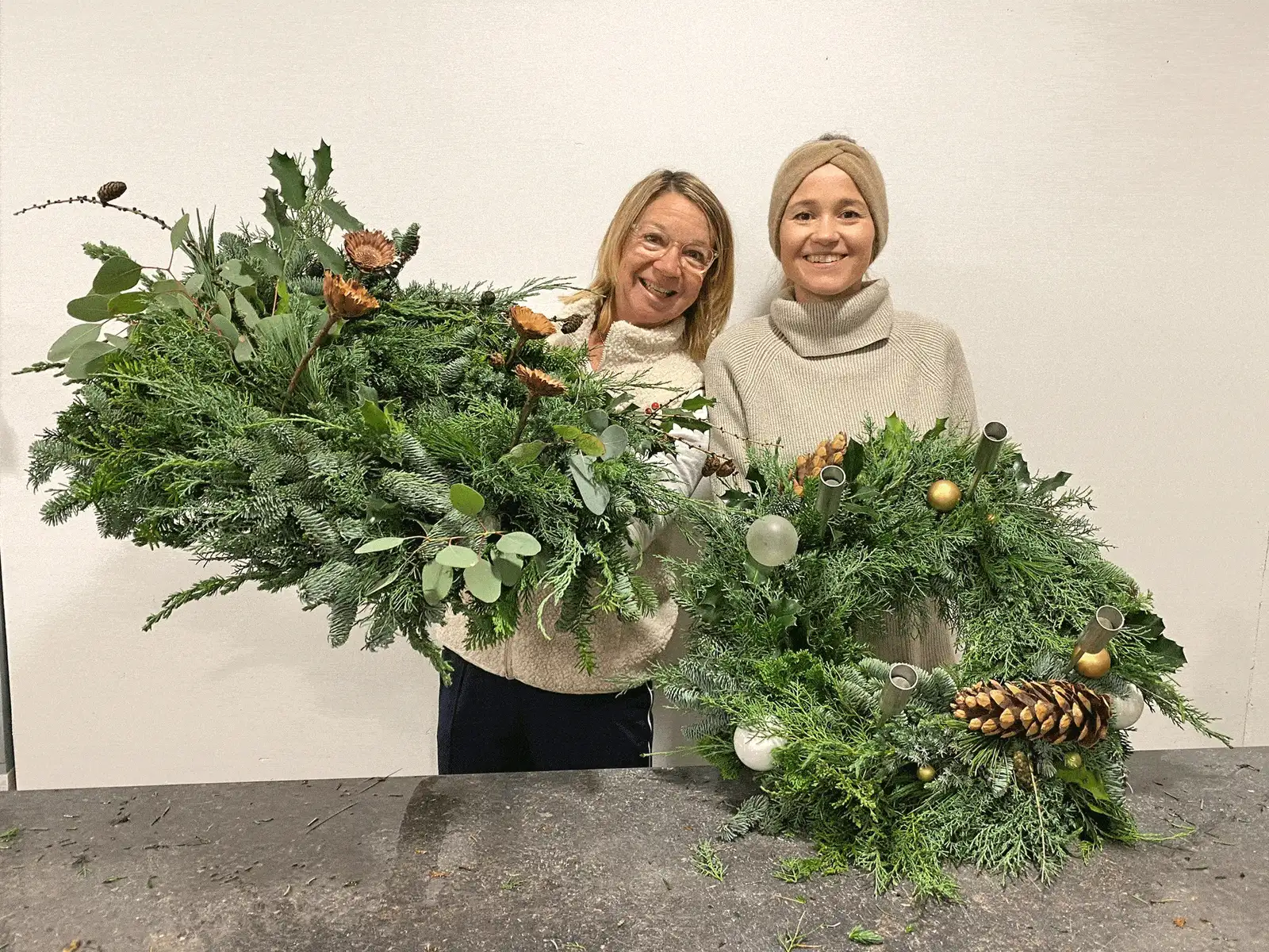Zwei Floristinnen präsentieren großen Weihnachtskranz mit Zapfen, Kugeln und Grünwerk