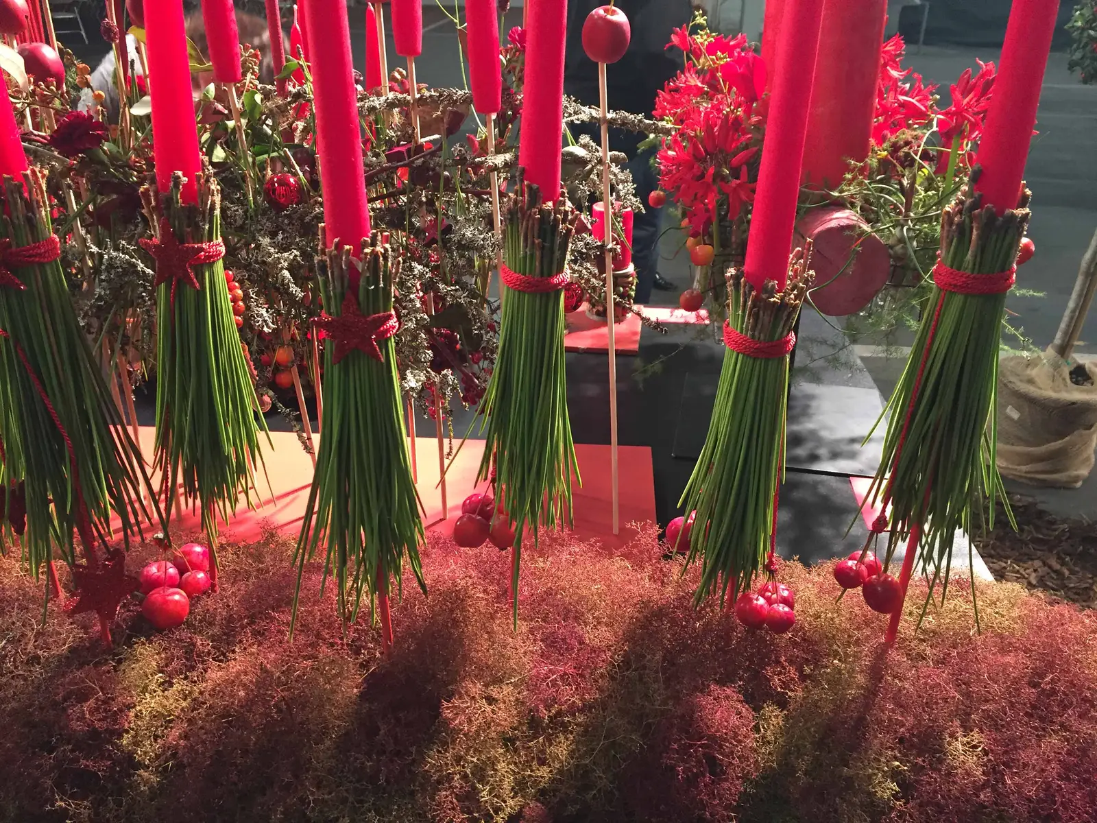Installationsfoto: Viele Blumenbündel mit roten Bändern und Kugeln im Sand, Ausstellungsarrangement