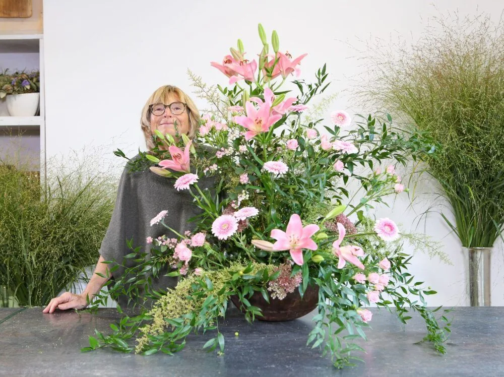 Floristin mit üppiger, pompöser Blumengestaltung in Brauntönen mit Lilien, Gerberas und Grünwerk