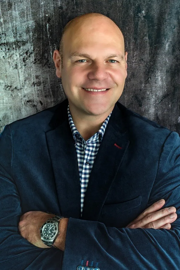 Ingo Steinbock, Autor des Flugangst Coaching Masterkurses, in dunklem Blazer vor strukturierter grauer Wand