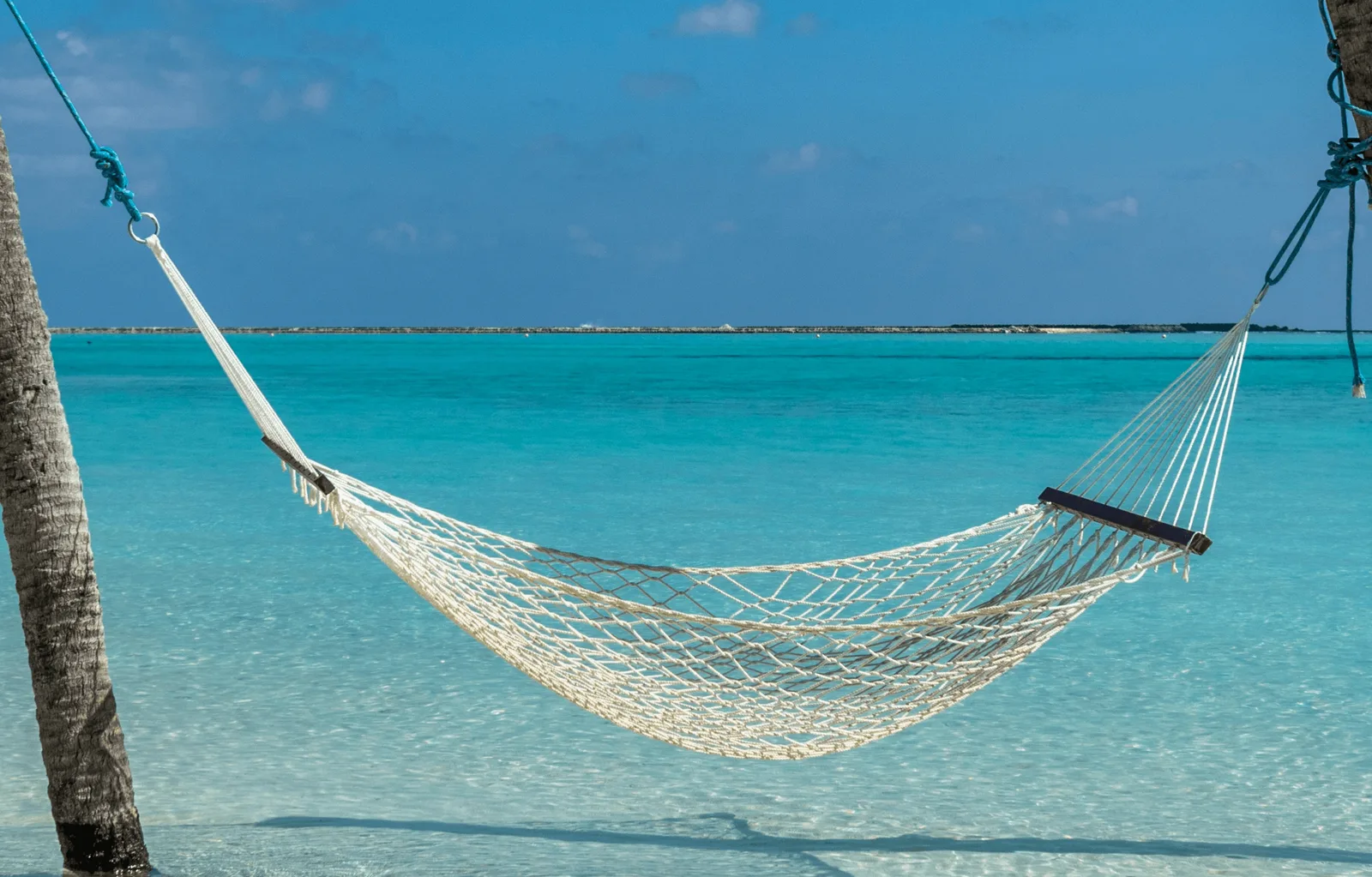 Hängematte am tropischen Strand mit türkisblauem Meer und Palmenstamm