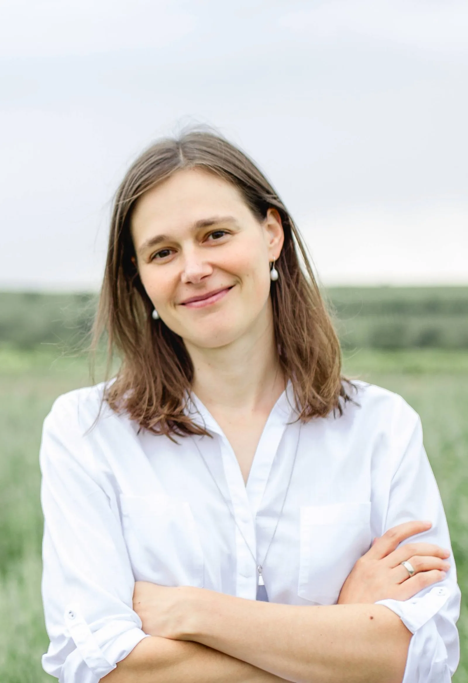 Lena Franck in weißem Hemd vor grünem Feld, Porträt mit verschränkten Armen