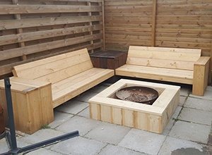 Holz-Sitzbänke mit quadratischem Feuerkorb in der Mitte auf Pflastersteinen