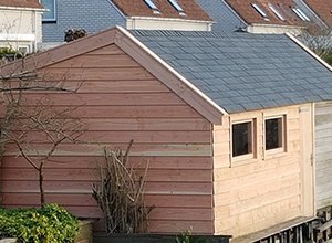 Braunes Gartenhaus mit grauem Dach und Fenster im Hintergrund