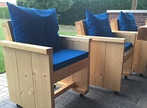 Zwei braune Holzsessel mit blauen Sitzkissen auf Terrassenboden