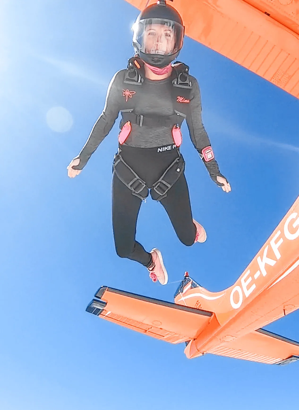Frau in Fallschirmsprung-Ausrüstung springt aus Flugzeug mit orangem Fallschirm