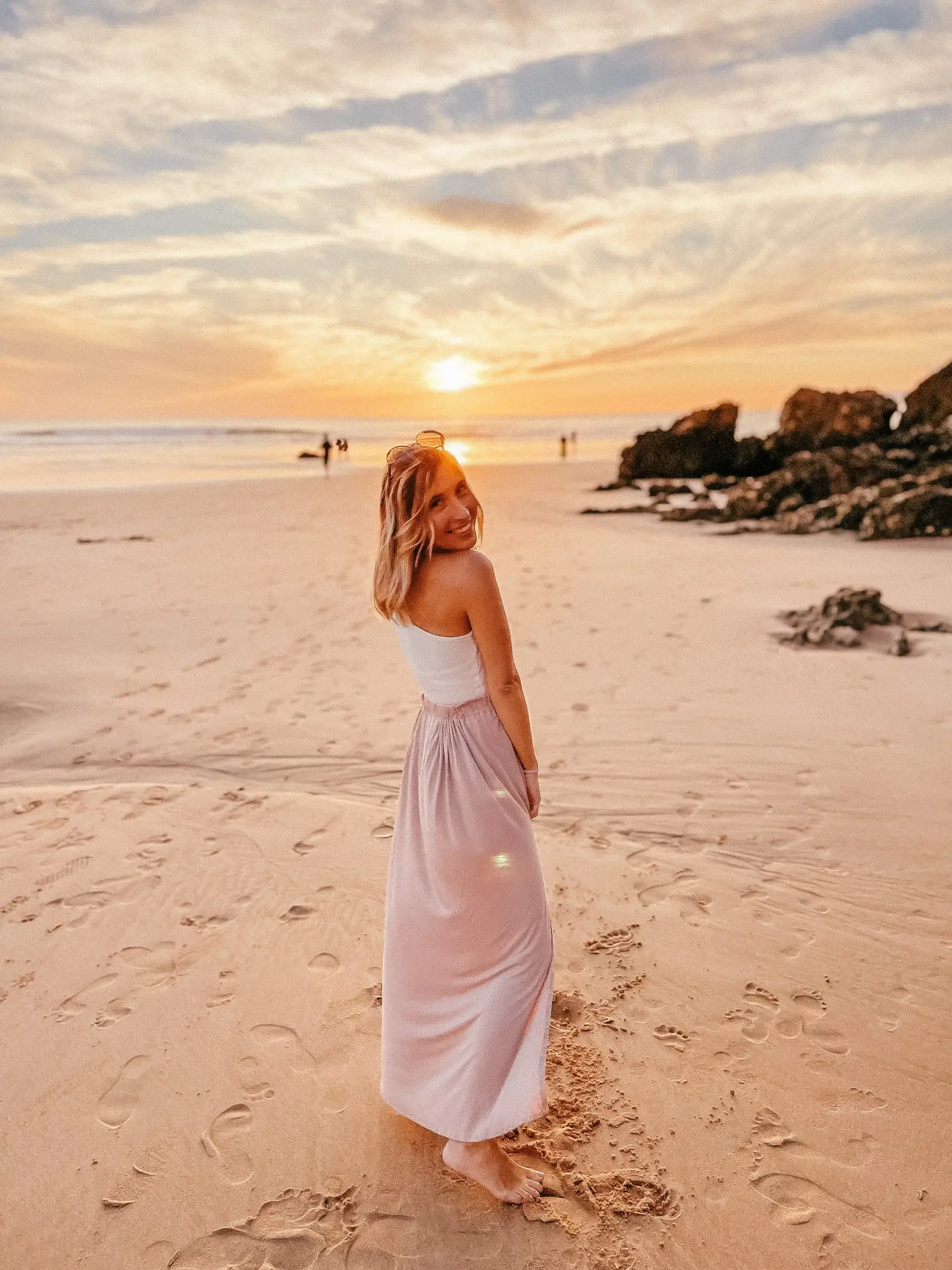 Frau in weißem Top und rosa Rock am Strand bei Sonnenuntergang