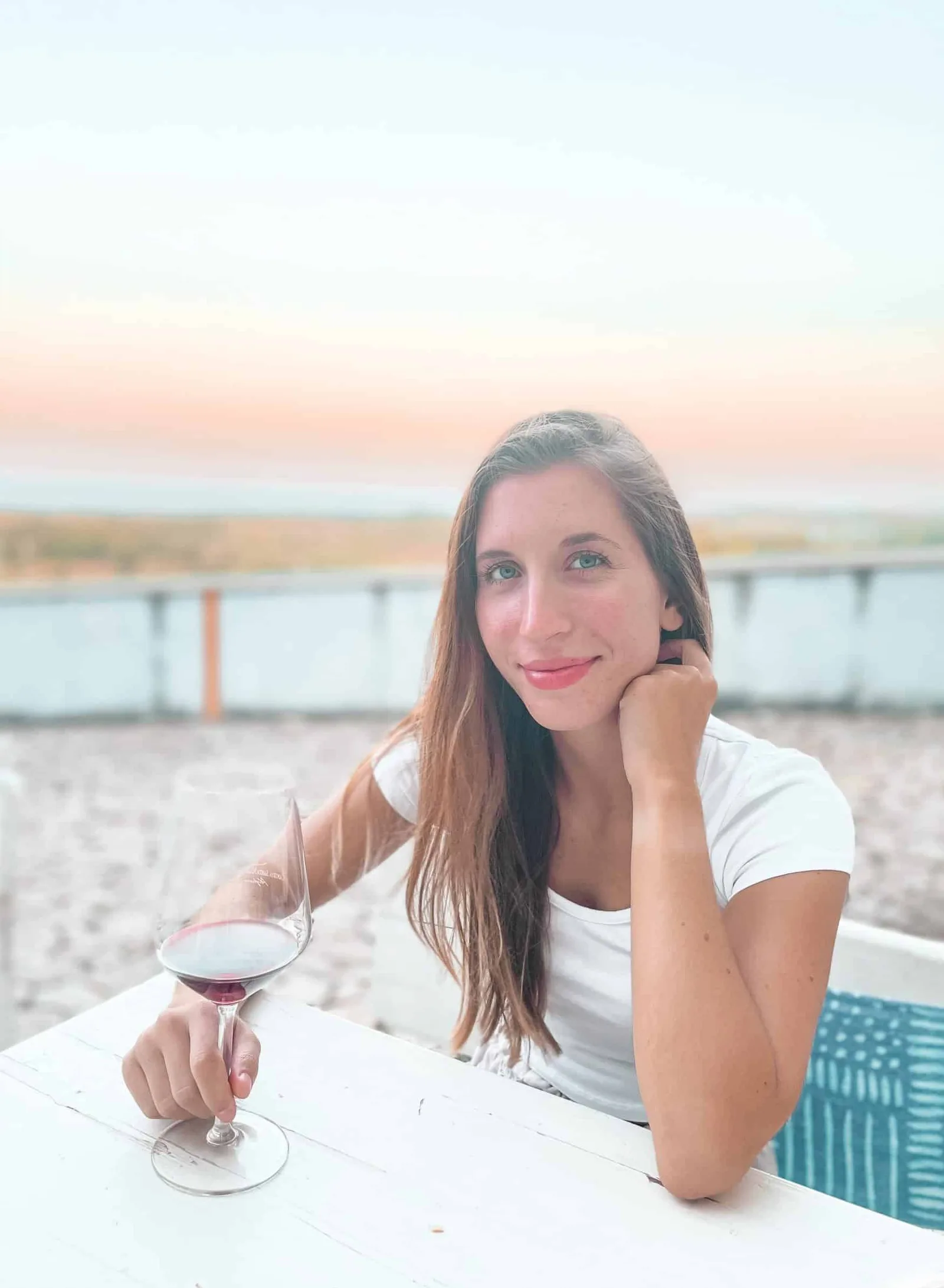Frau mit rötlichem Haar am Strand mit Getränk, Sonnenuntergang im Hintergrund