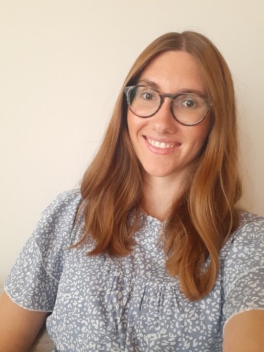 Frau mit rötlichem Haar und Brille in grauem Leoparden-Print Shirt, lächelnd