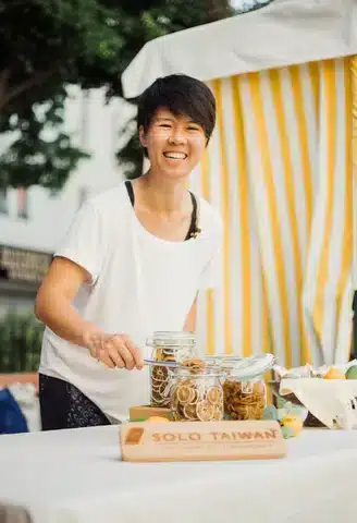 Junge Frau mit dunklen Haaren in weißem Shirt, Getränkedose, Solo Taiwan Schild