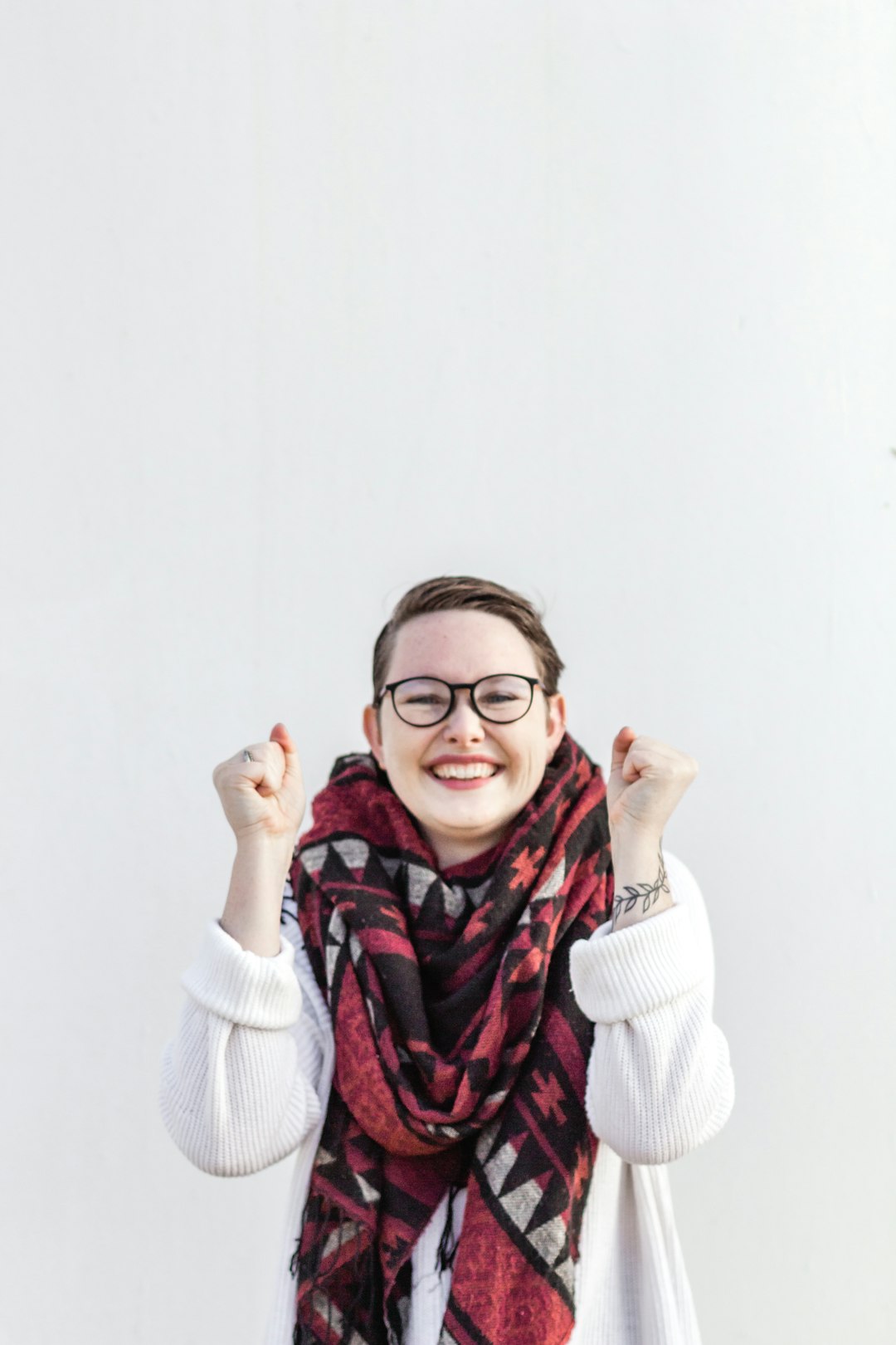 Junges Mädchen mit Brille und kariertem Schal macht Freudengeste vor weißem Hintergrund